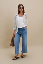 Woman wearing a striped shirt, white tank top, blue jeans, and black sandals on a beige background | model-size: 4