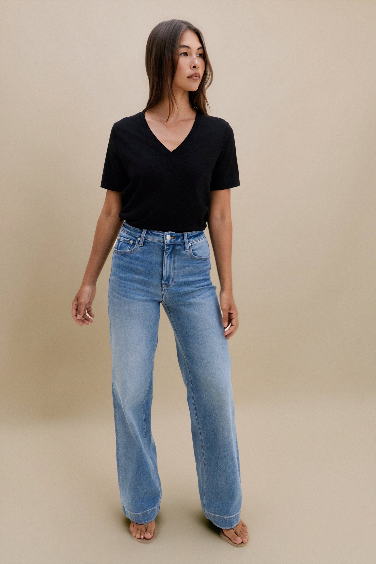 Woman wearing a black top and blue jeans against a beige background 