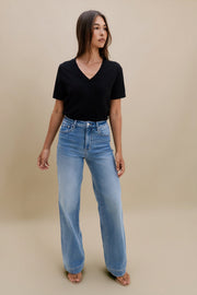 Woman wearing a black top and blue jeans against a beige background 