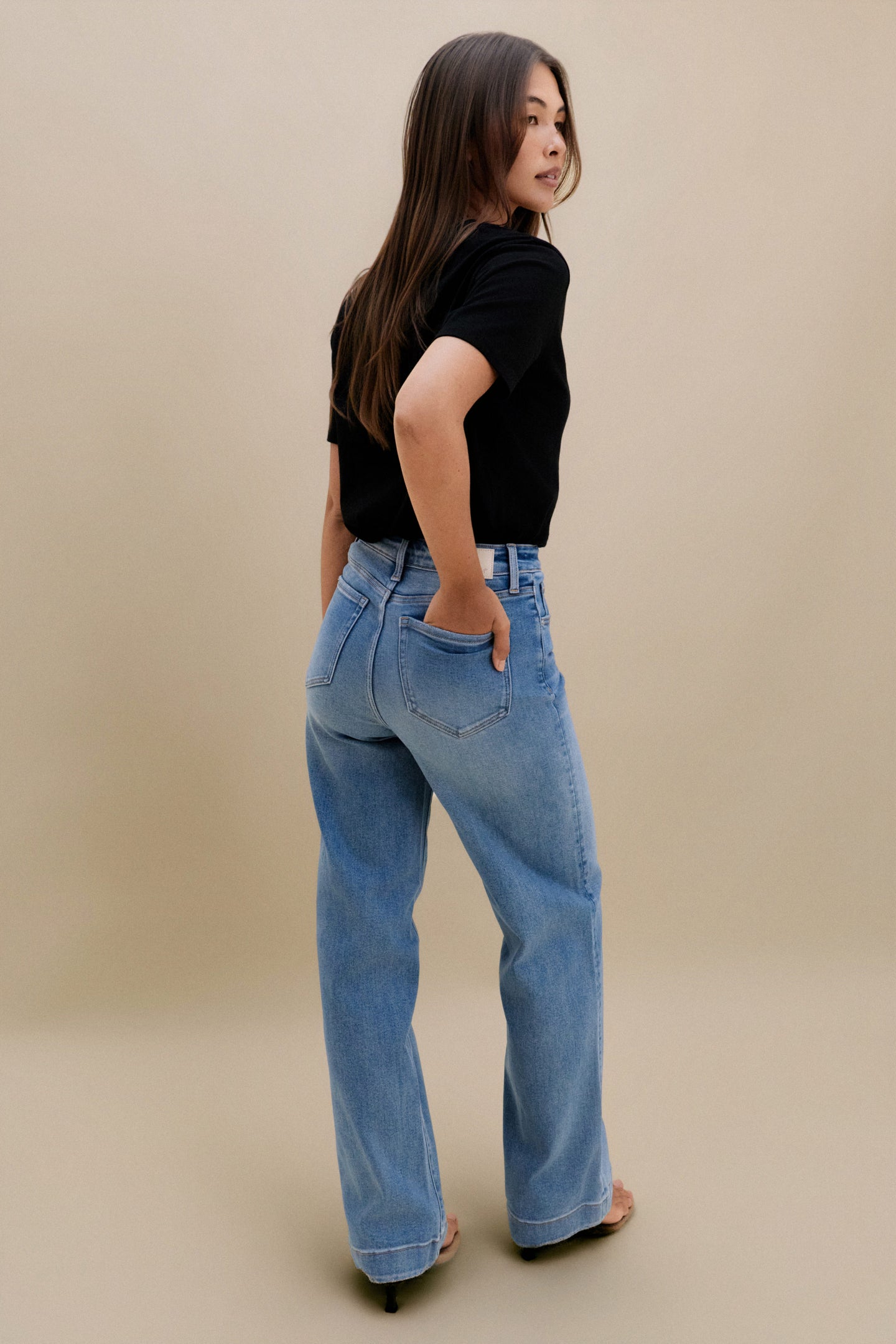 Woman wearing blue jeans and a black top on a beige background