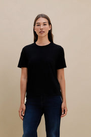 Woman wearing a black crew neck t-shirt and blue jeans standing in front of a beige wall | model-size: 4