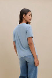 Woman wearing a light blue t-shirt and jeans against a beige background 