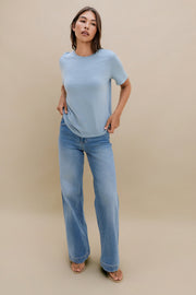 Woman wearing a light blue t-shirt and jeans against a beige background 