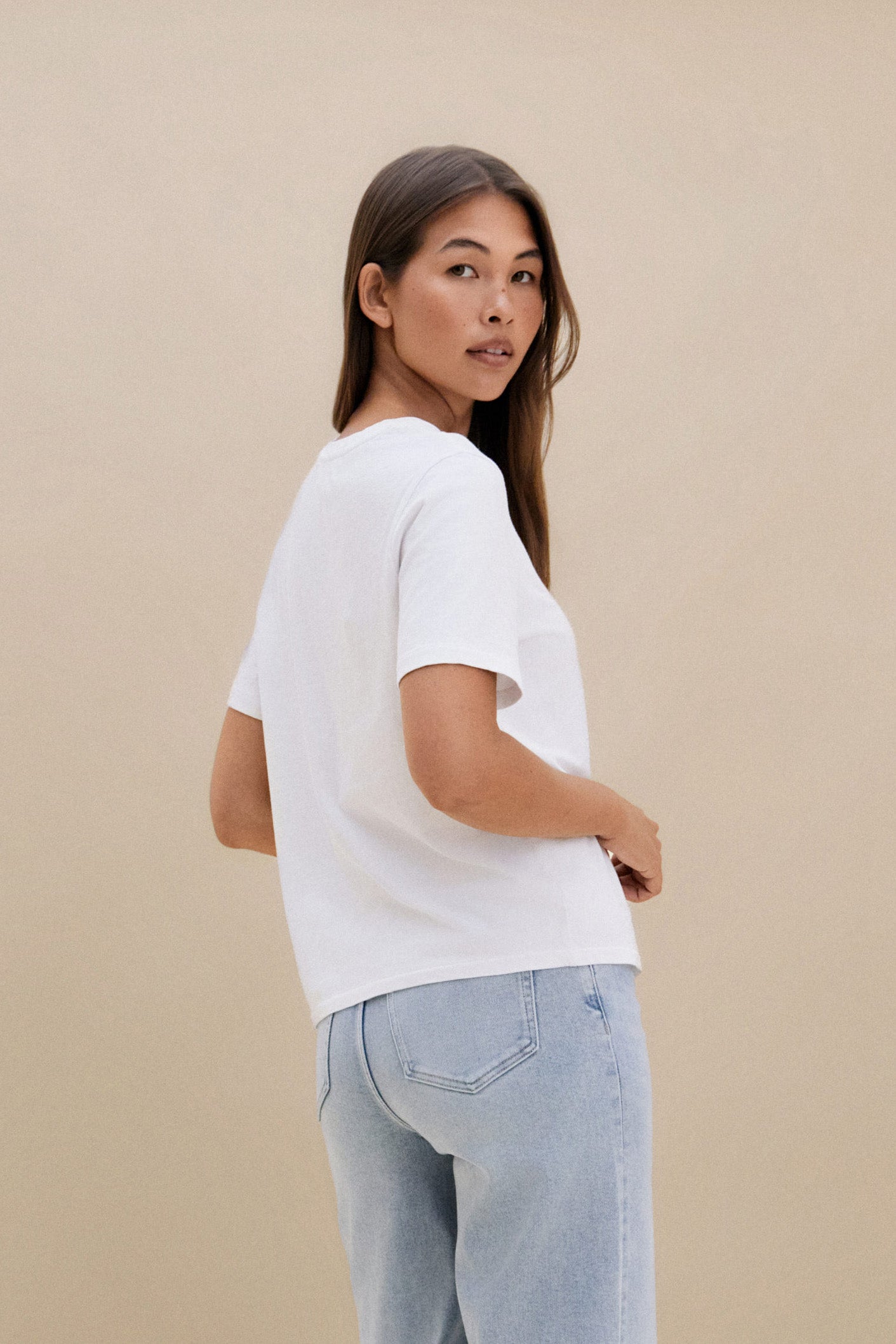 Woman wearing a plain white t-shirt and blue jeans against a beige background