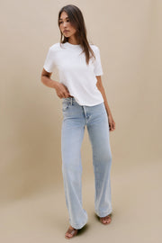 Woman wearing a plain white t-shirt and blue jeans against a beige background