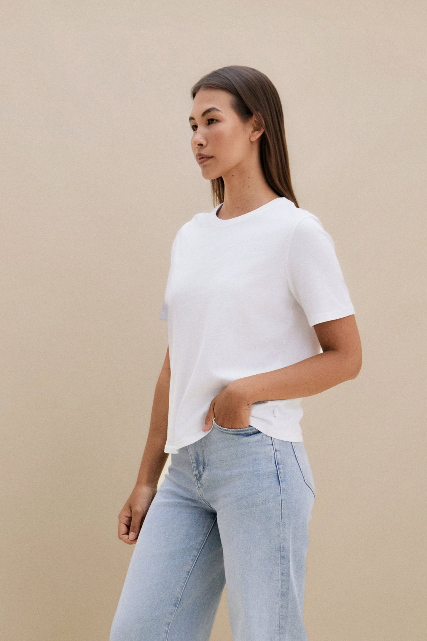 Woman wearing a plain white t-shirt and blue jeans against a beige background