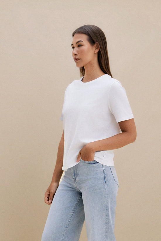 Woman wearing a plain white t-shirt and blue jeans against a beige background