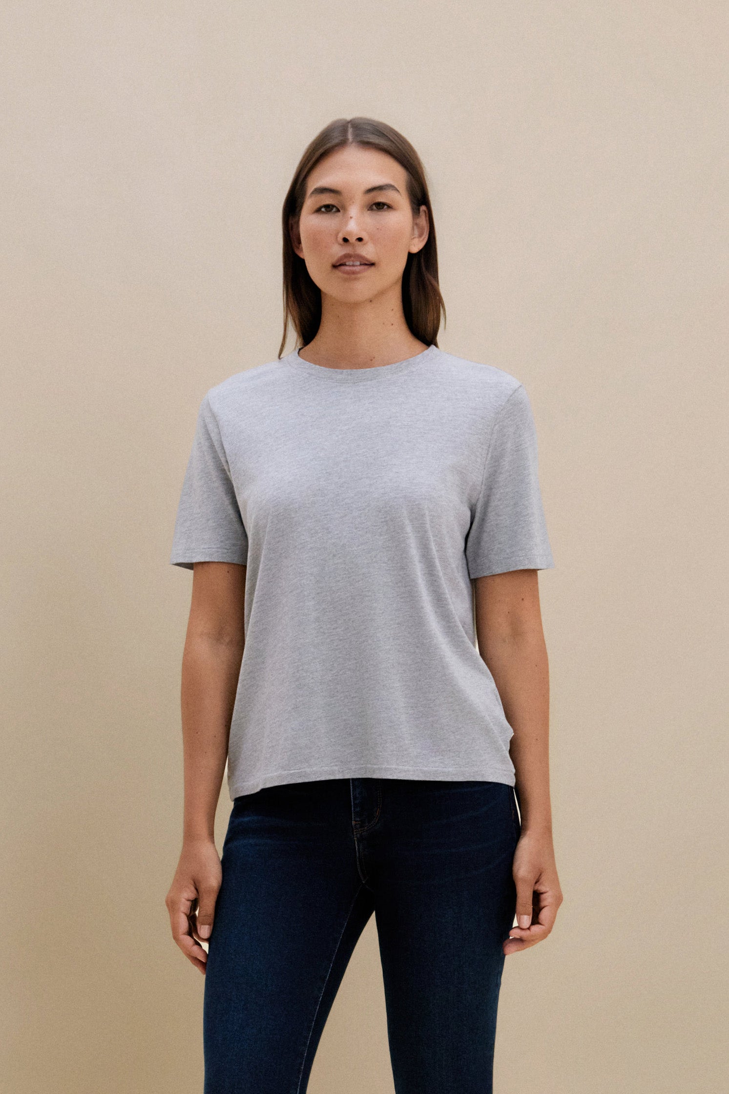 Woman wearing a gray t-shirt and dark pants against a beige background | model-size: 4