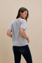 Woman wearing a gray t-shirt and dark jeans against a beige background
