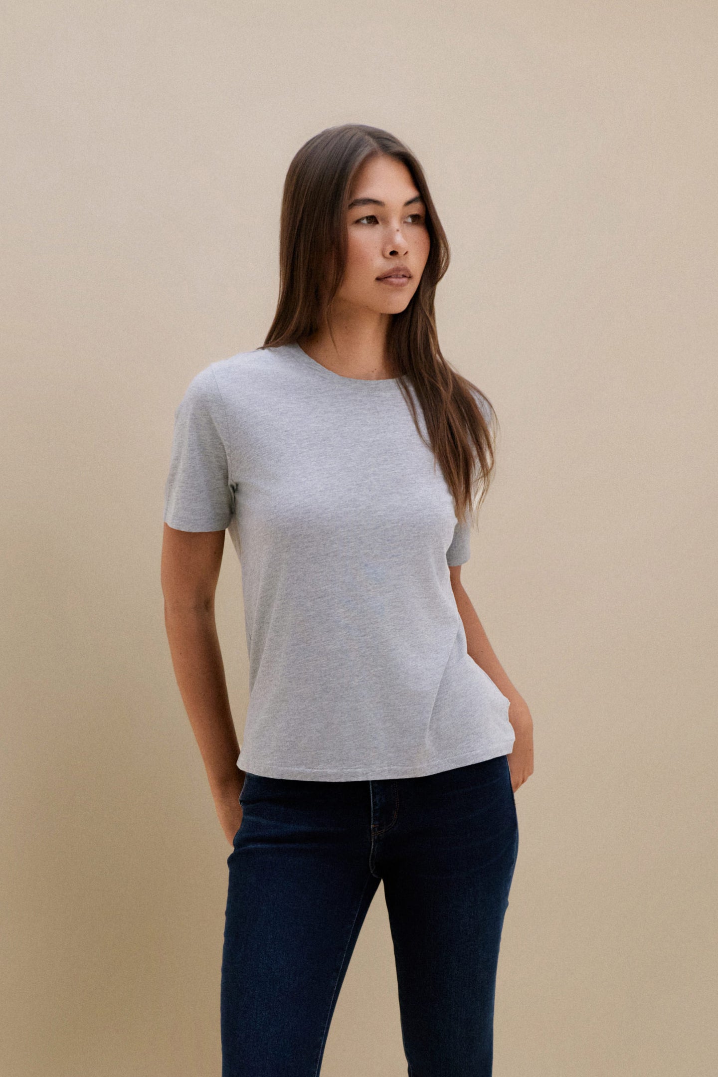 Woman wearing a gray t-shirt and dark jeans against a beige background