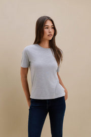 Woman wearing a gray t-shirt and dark jeans against a beige background