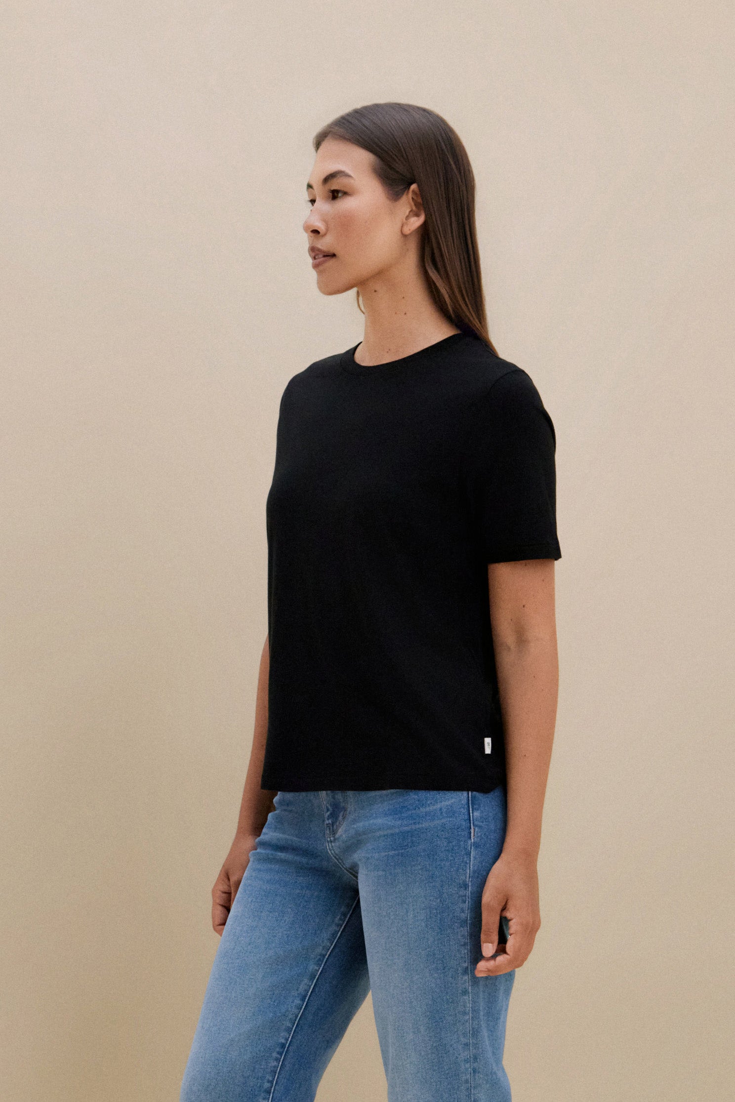 Woman wearing a black t-shirt and blue jeans against a beige background
