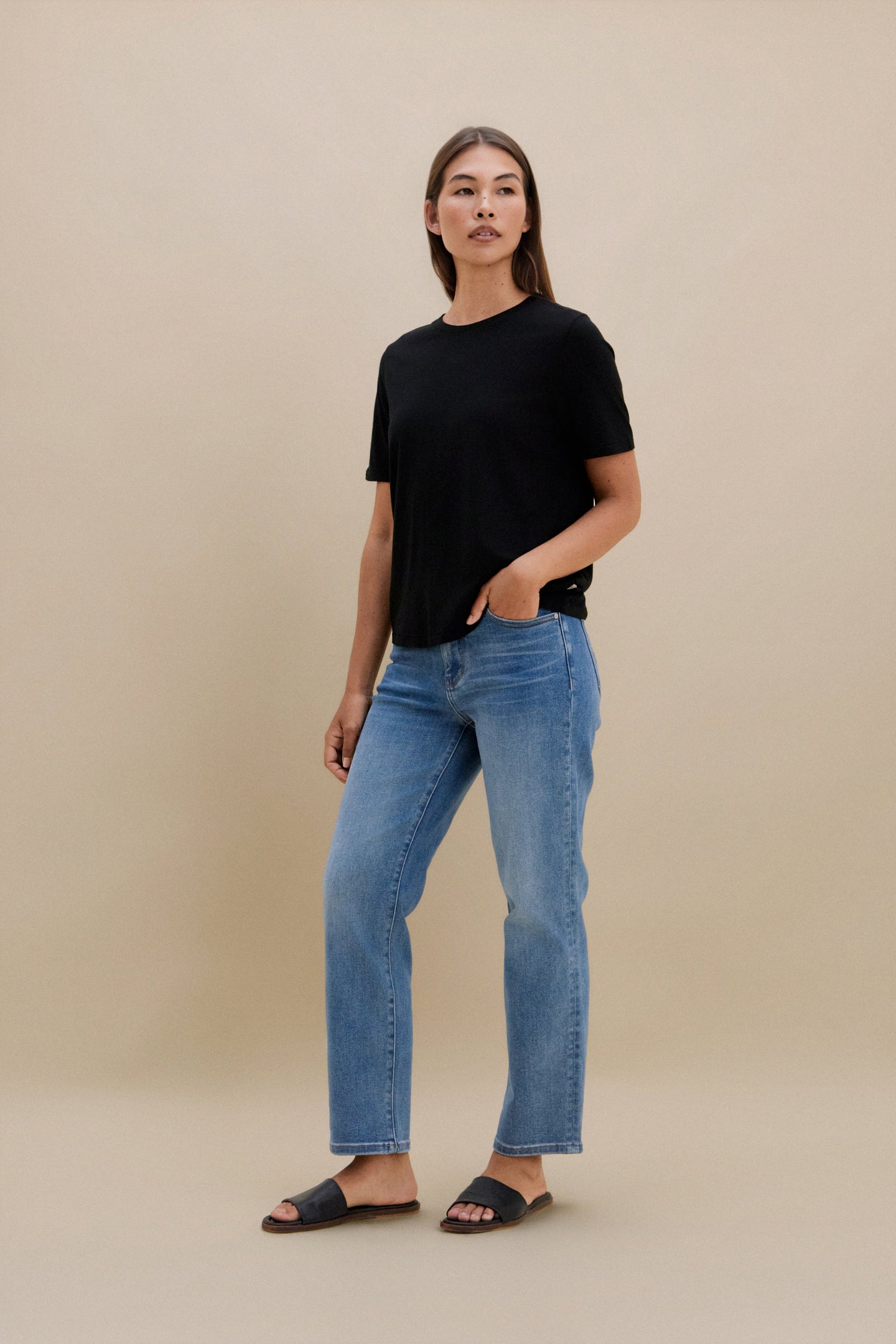 Woman wearing a black t-shirt and blue jeans against a beige background