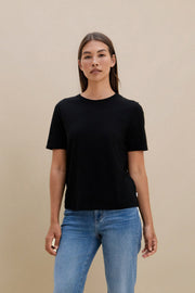 Woman wearing a black t-shirt and blue jeans against a beige background | model-size: 4