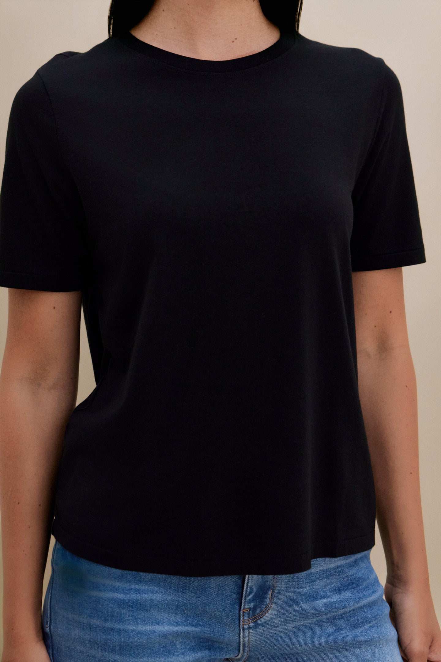 Woman wearing a black t-shirt and blue jeans against a beige background