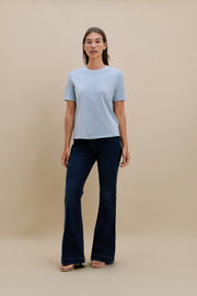 Woman wearing a light blue t-shirt and dark jeans against a beige background