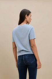 Woman wearing a light blue t-shirt and dark jeans against a beige background