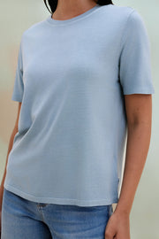 Woman wearing a light blue t-shirt and jeans against a beige background 