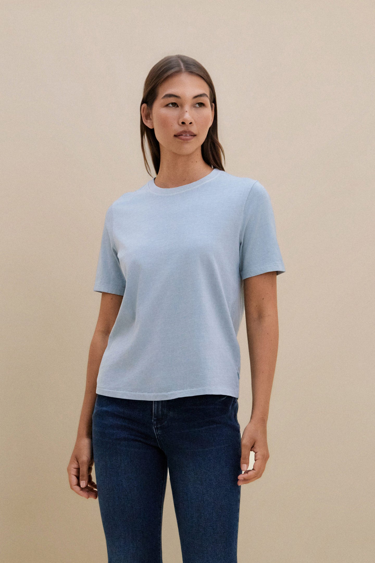Woman wearing a light blue t-shirt and dark jeans against a beige background | model-size: 4