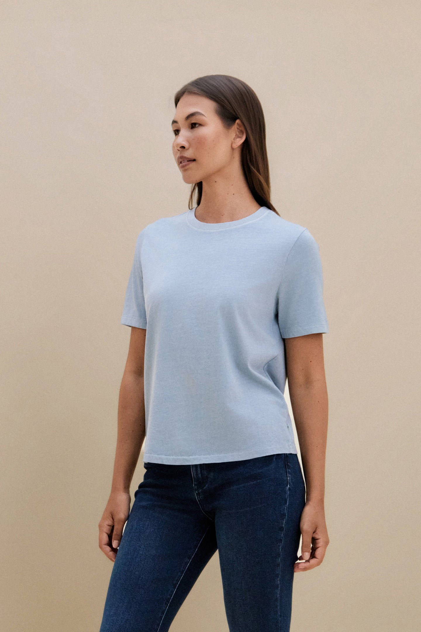 Woman wearing a light blue t-shirt and dark jeans against a beige background