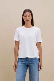 Woman wearing a white t-shirt and blue jeans with a beige background 