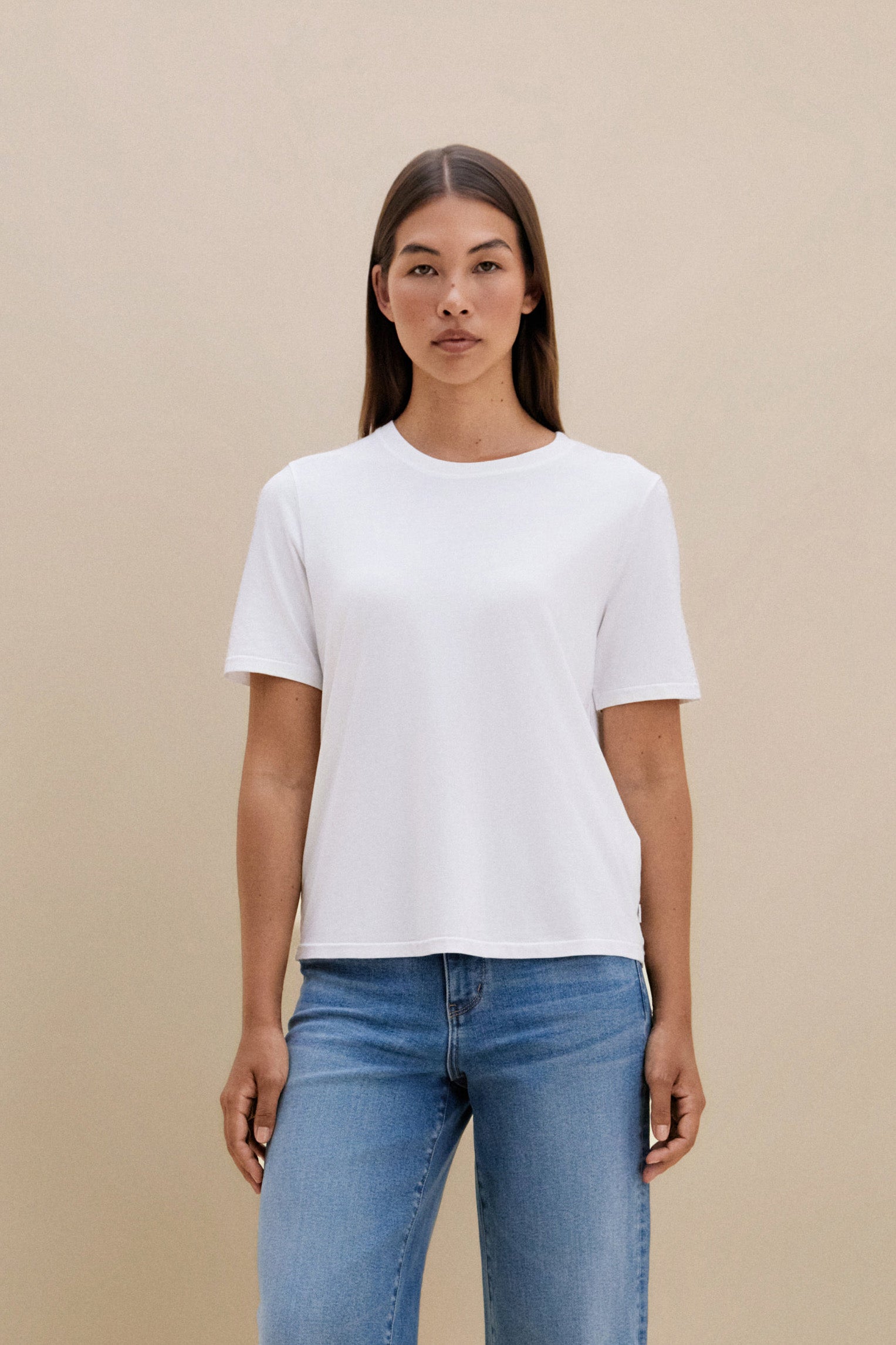 Woman wearing a white t-shirt and blue jeans with a beige background 