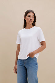 Woman wearing a white t-shirt and blue jeans with a beige background | model-size: 4