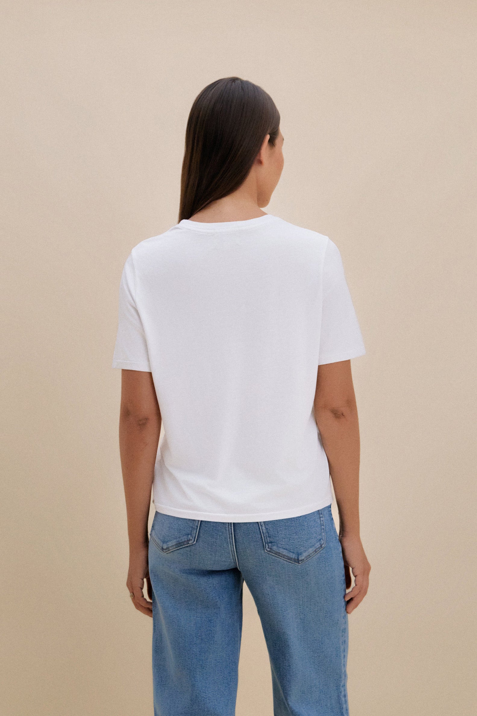Woman wearing a white t-shirt and blue jeans with a beige background 