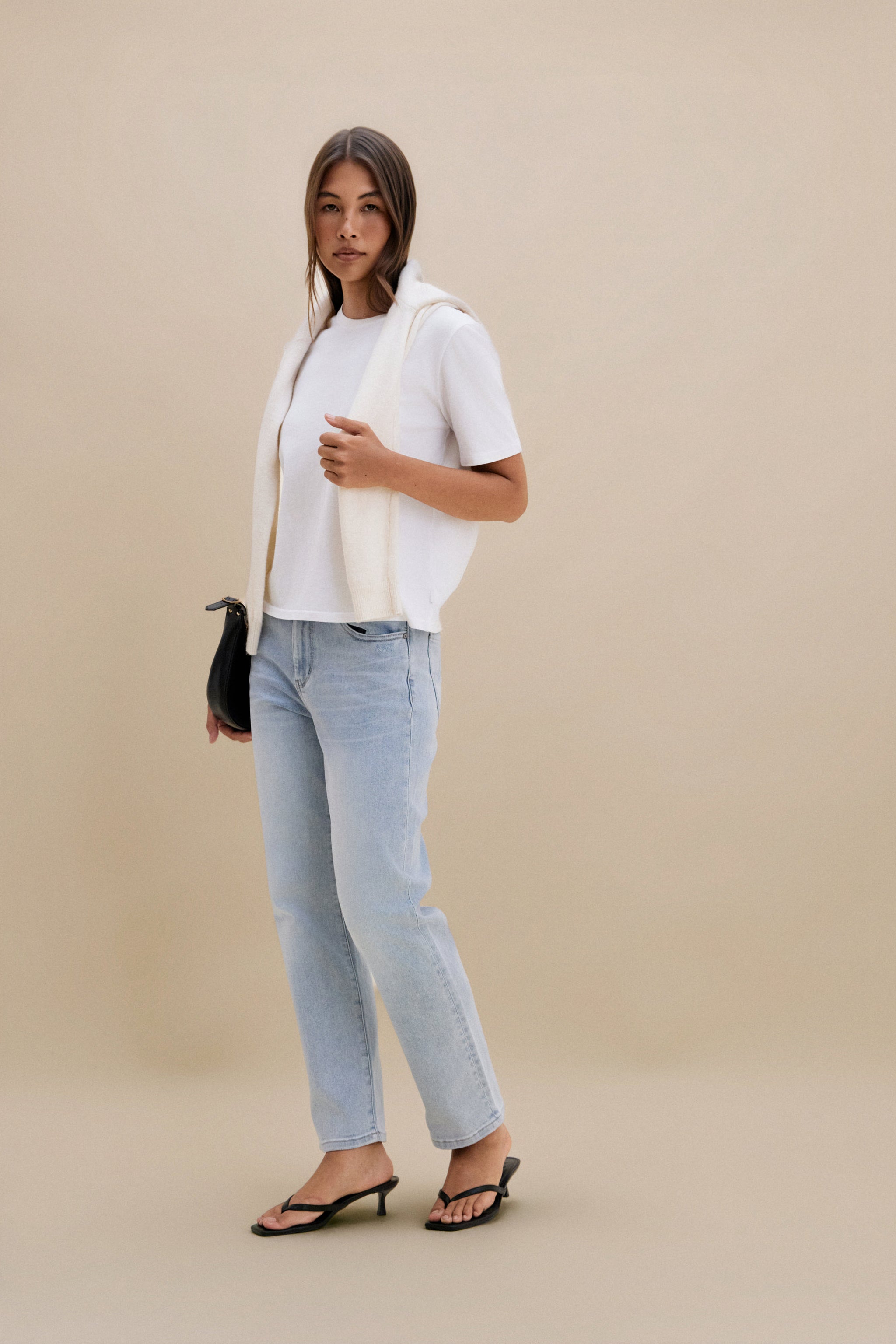 Woman wearing a plain white t-shirt and blue jeans against a beige background