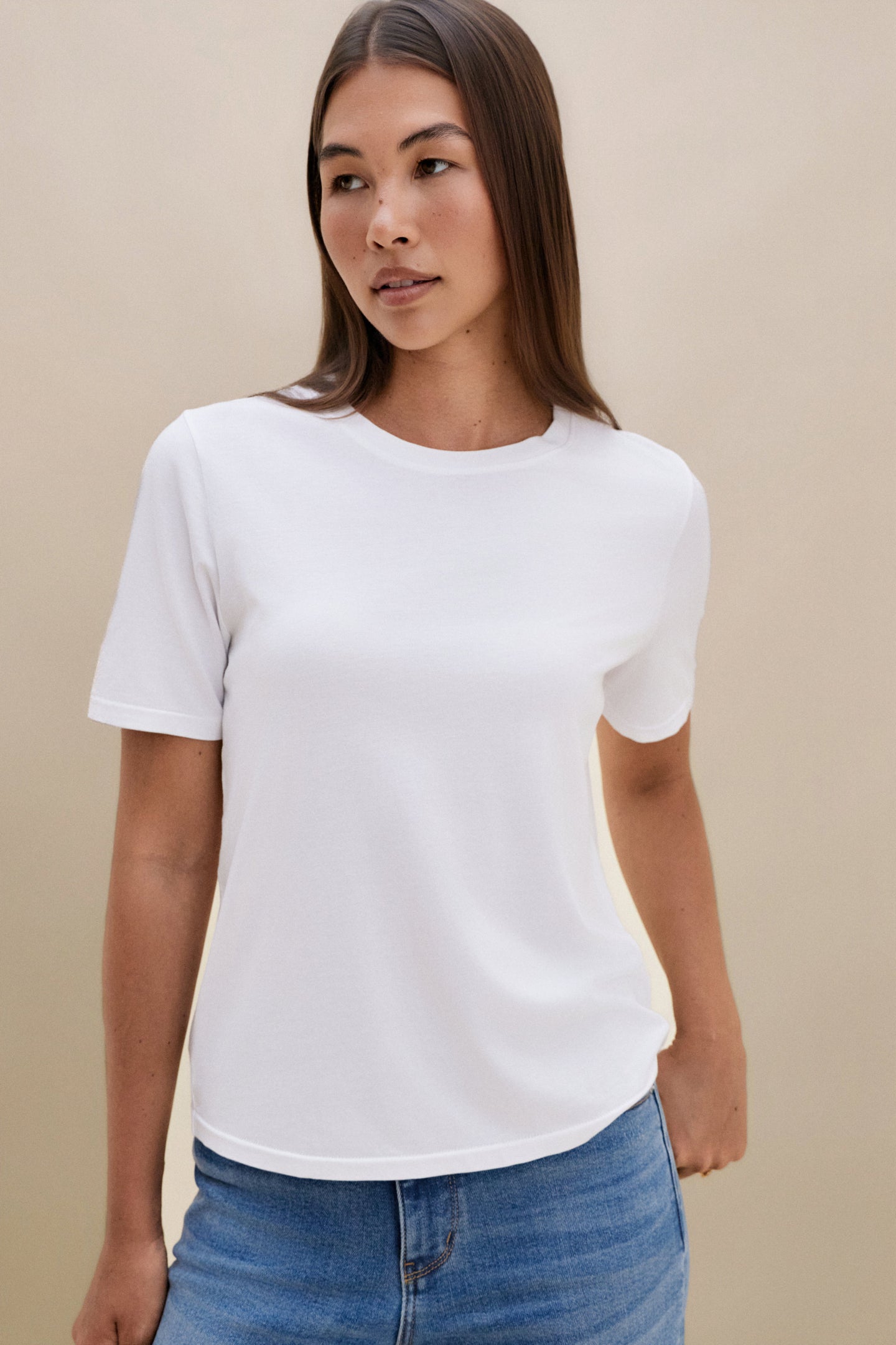 Woman wearing a white t-shirt and blue jeans with a beige background 