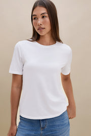 Woman wearing a white t-shirt and blue jeans with a beige background 
