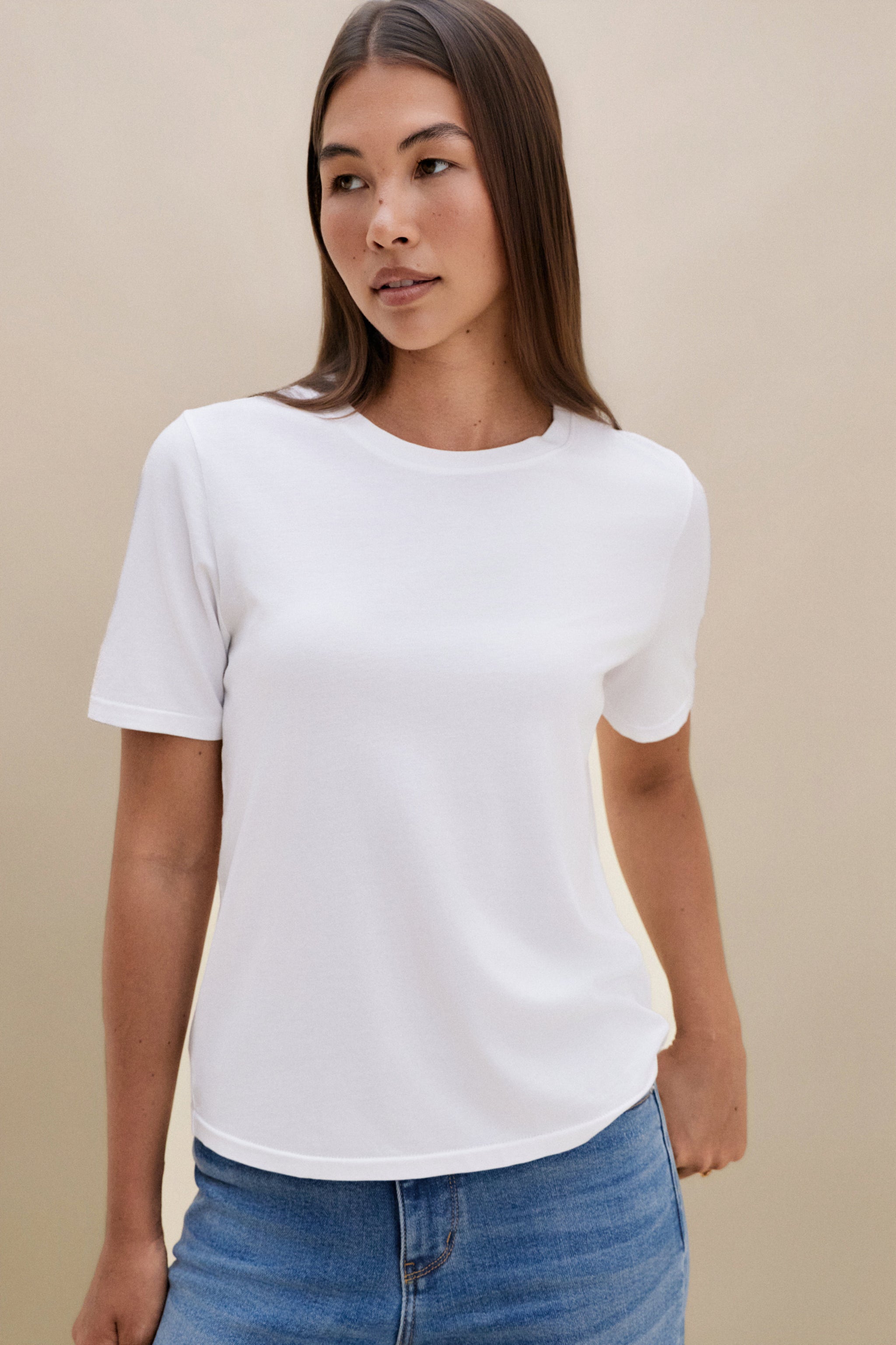 Woman wearing a white t-shirt and blue jeans with a beige background 