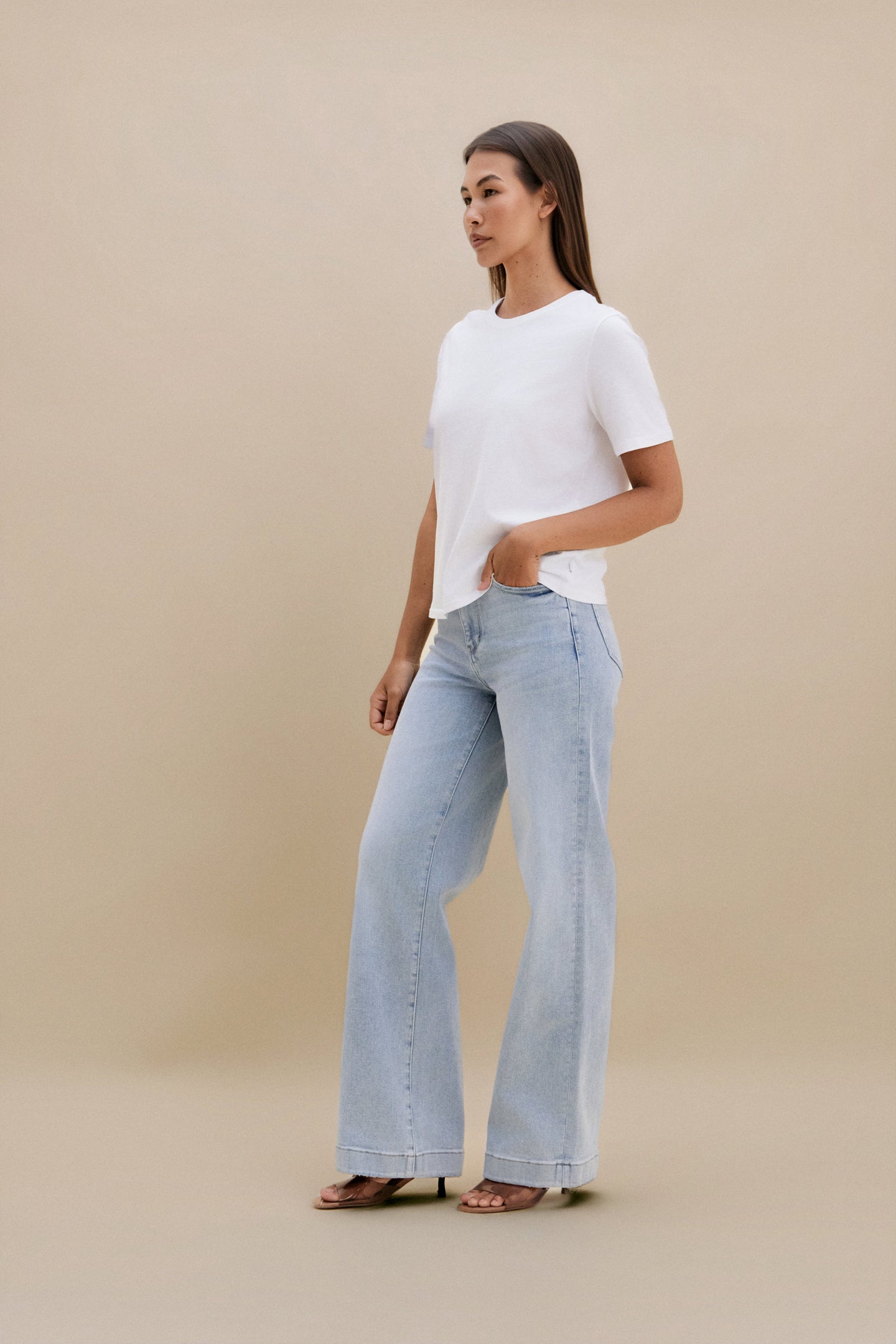 Woman wearing a white t-shirt and light blue jeans against a beige background