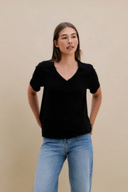 Woman wearing a black v-neck t-shirt and blue jeans against a beige wall | model-size: 4