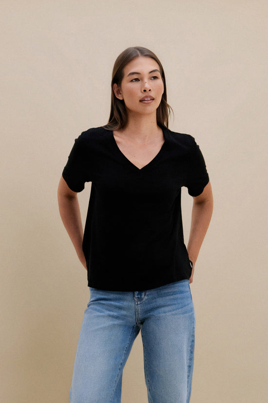 Woman wearing a black v-neck t-shirt and blue jeans against a beige wall | model-size: 4