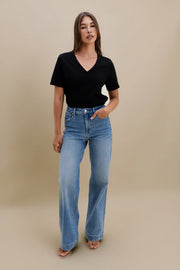 Woman wearing a black v-neck t-shirt and blue jeans against a beige wall 