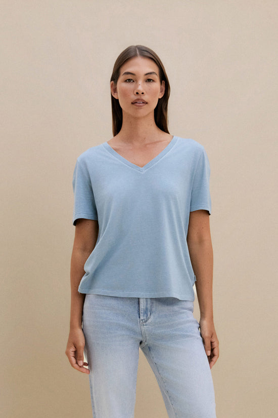 woman wearing light blue t-shirt and light colored denim with a beige wall 