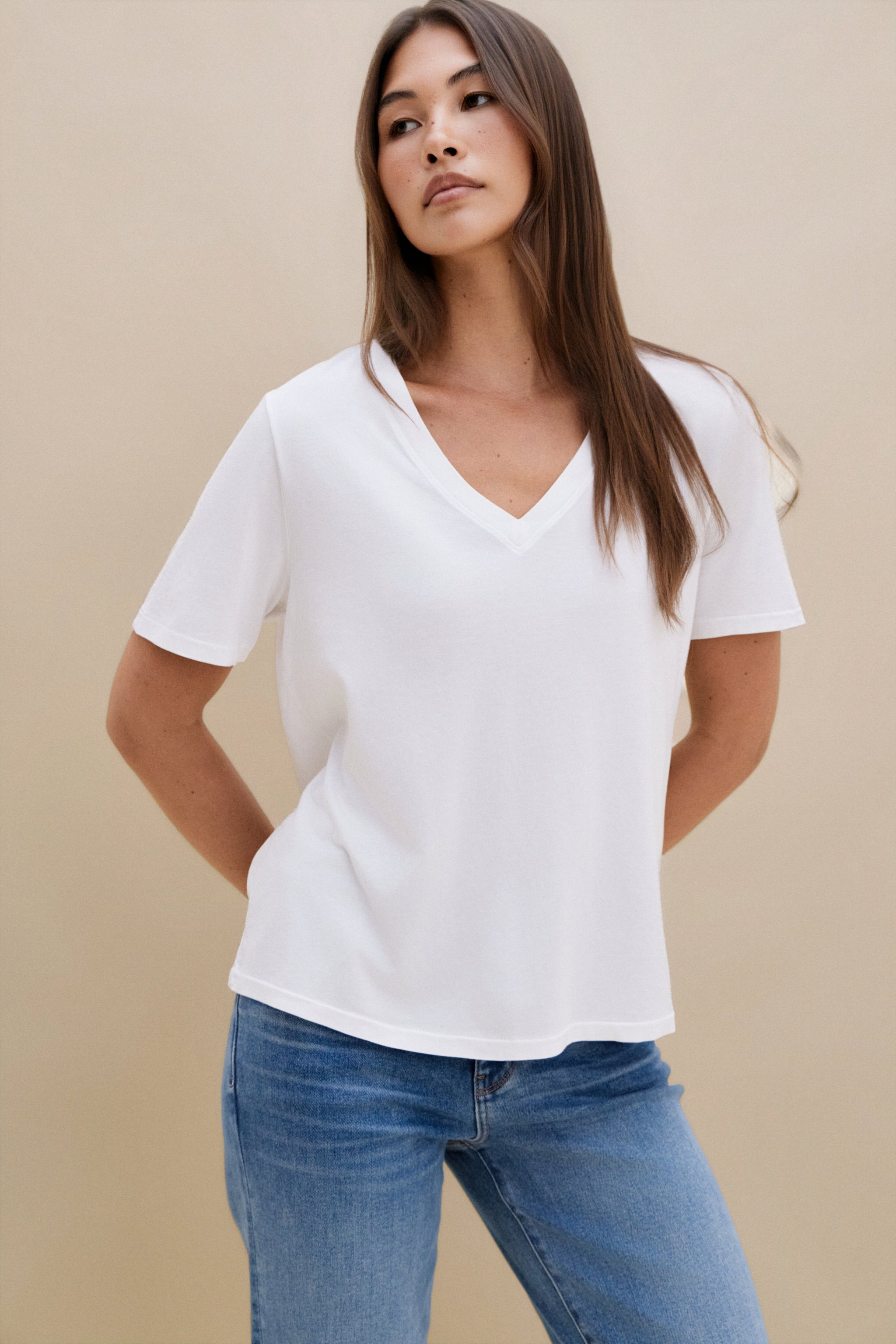 Woman wearing a white t-shirt, and blue jeans against a beige background | model-size: 4