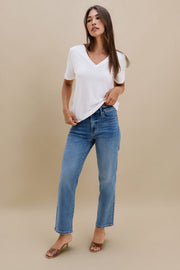Woman wearing a white t-shirt, and blue jeans against a beige background 