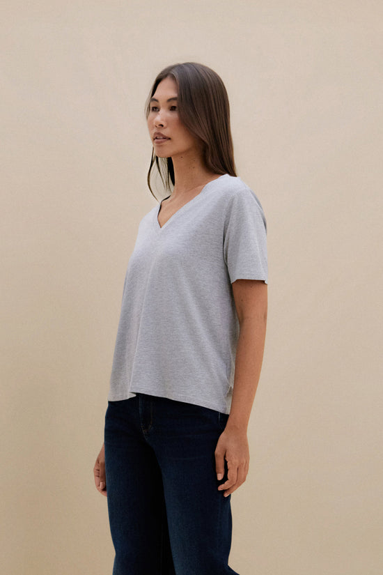 Woman wearing a gray t-shirt and dark jeans against a beige background