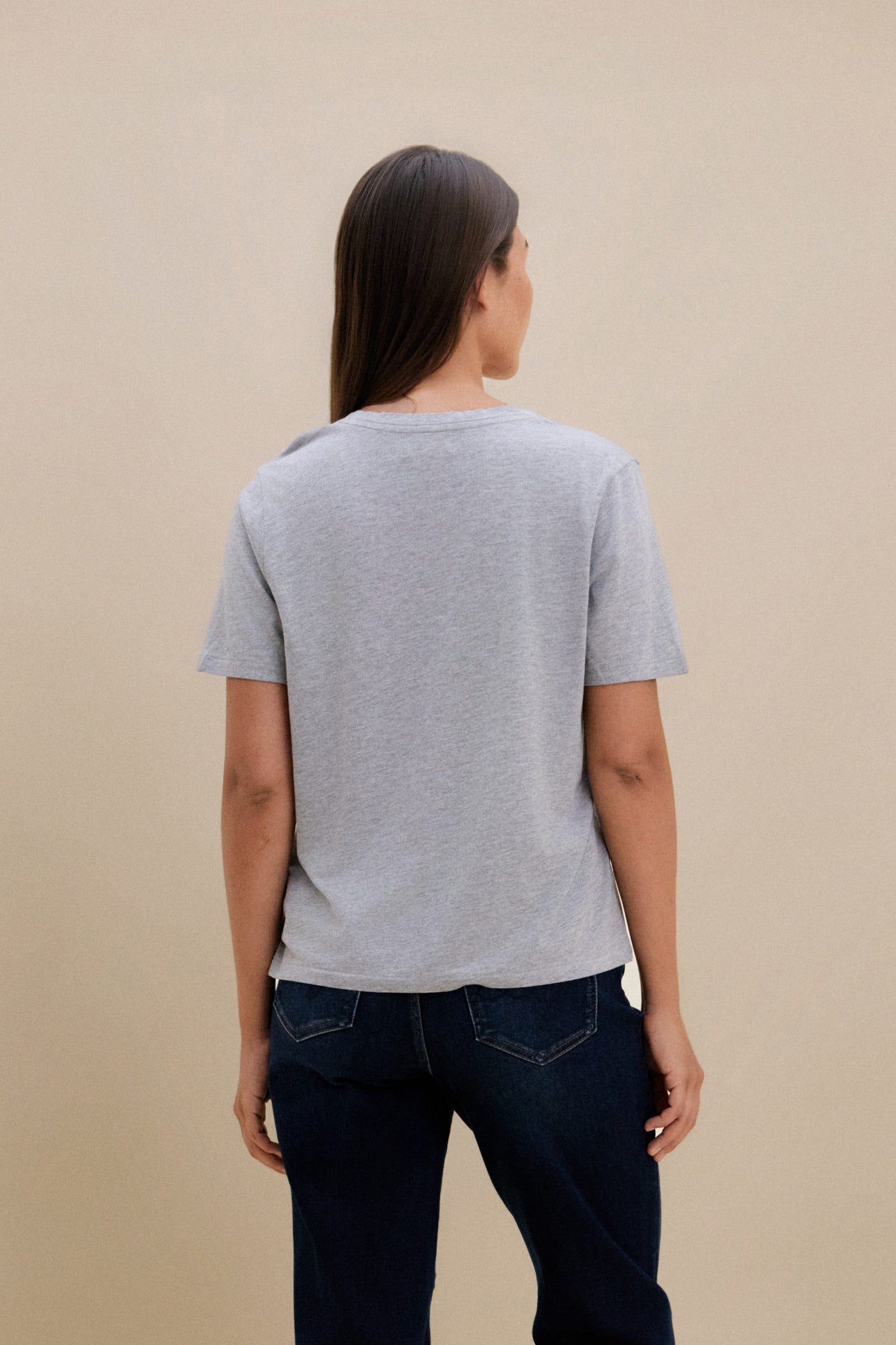 Person wearing a gray t-shirt and dark jeans against a beige background