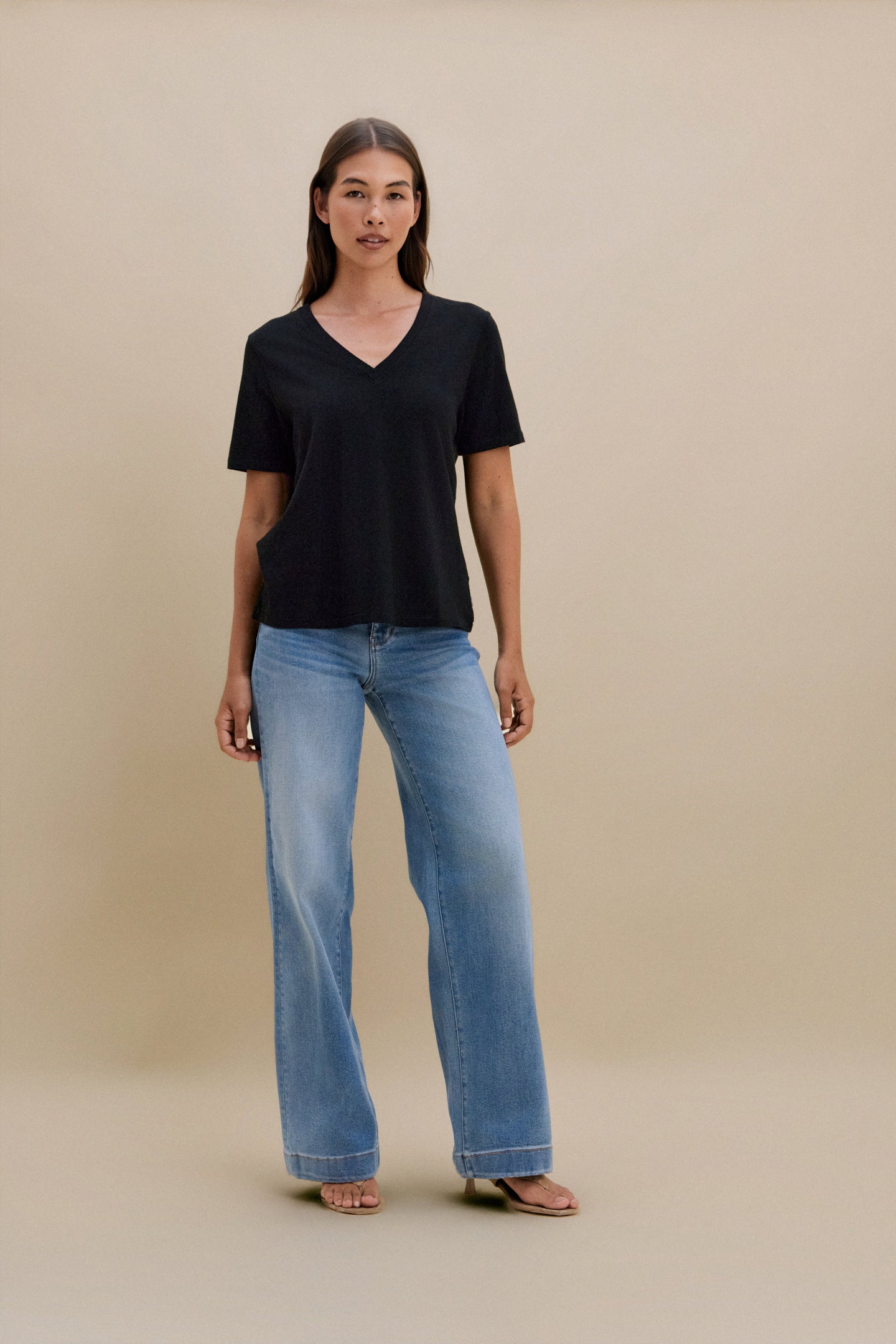 Woman wearing a black t-shirt and blue jeans on a beige background