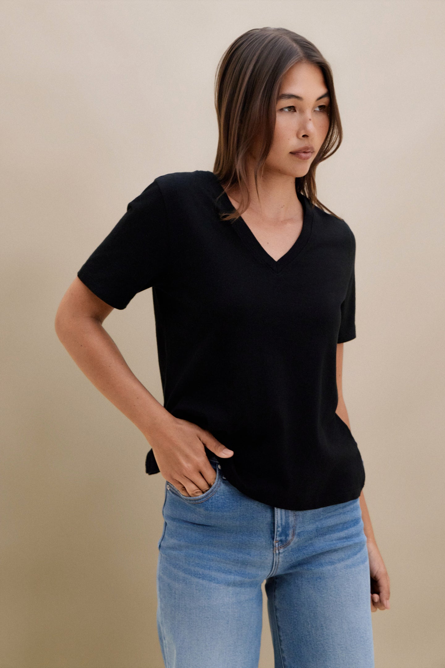 Woman wearing a black t-shirt and blue jeans against a beige background