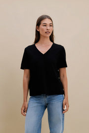 Woman wearing a black V-neck t-shirt and blue jeans against a beige background | model-size: 4