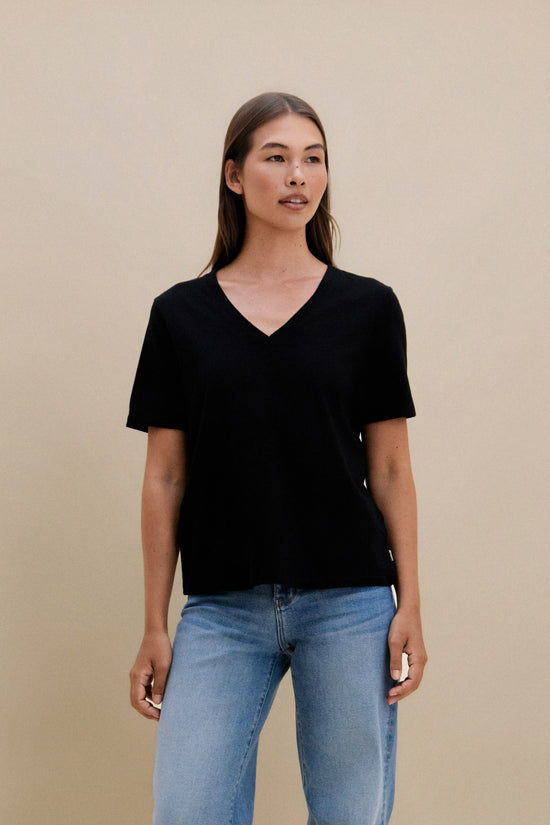Woman wearing a black V-neck t-shirt and blue jeans against a beige background | model-size: 4