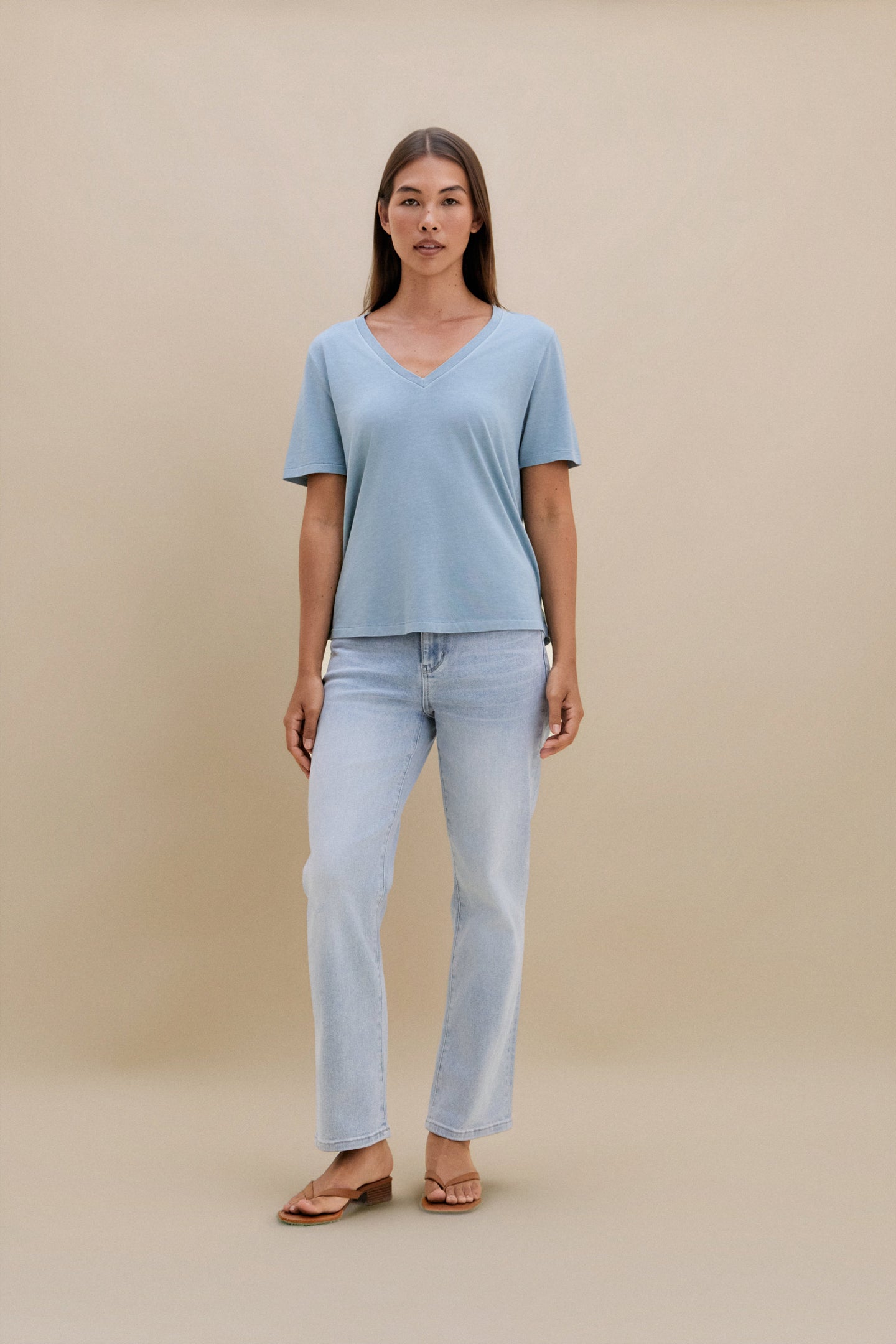 woman wearing light blue t-shirt and light colored denim with a beige wall 
