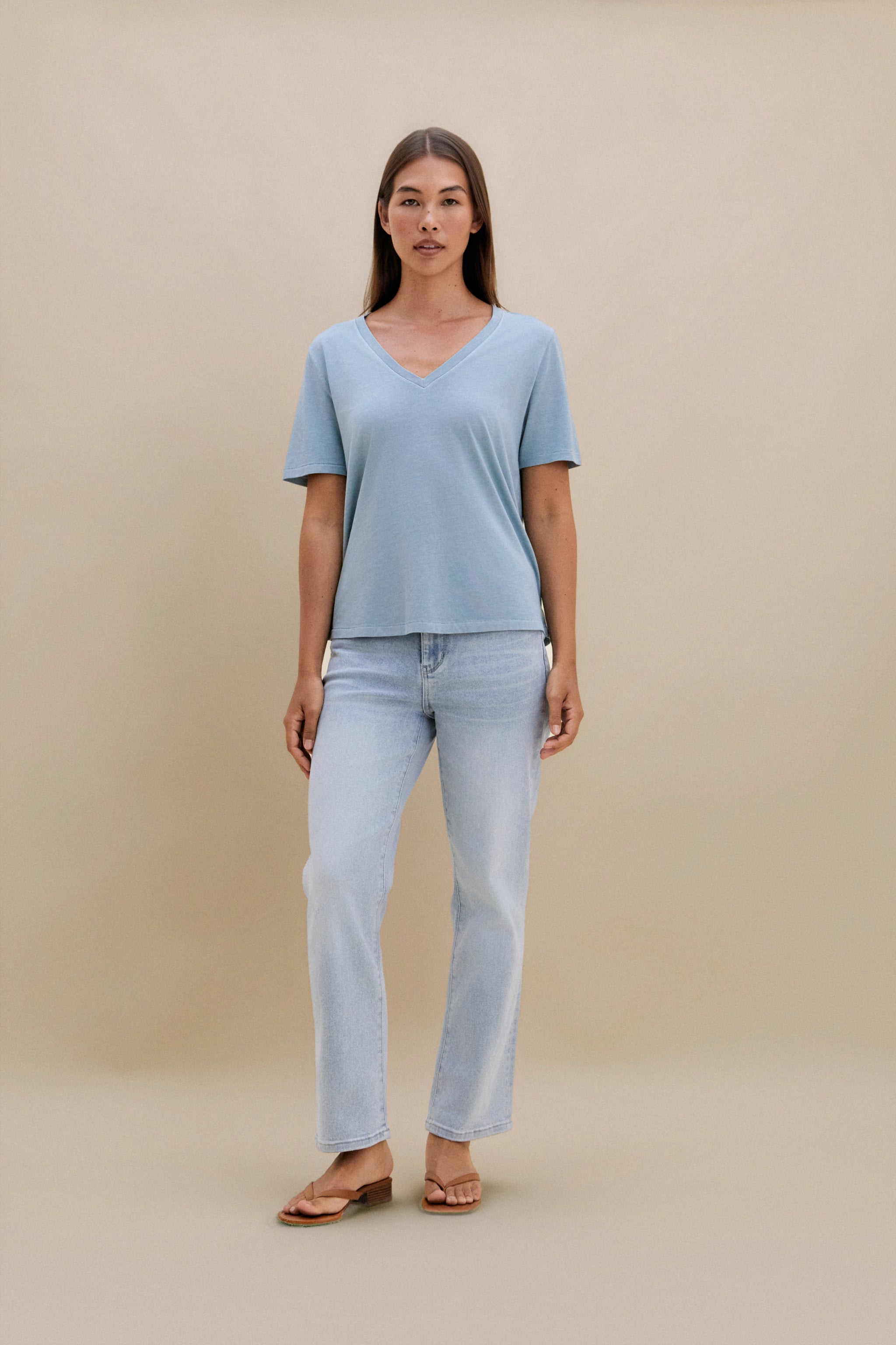 woman wearing light blue t-shirt and light colored denim with a beige wall 
