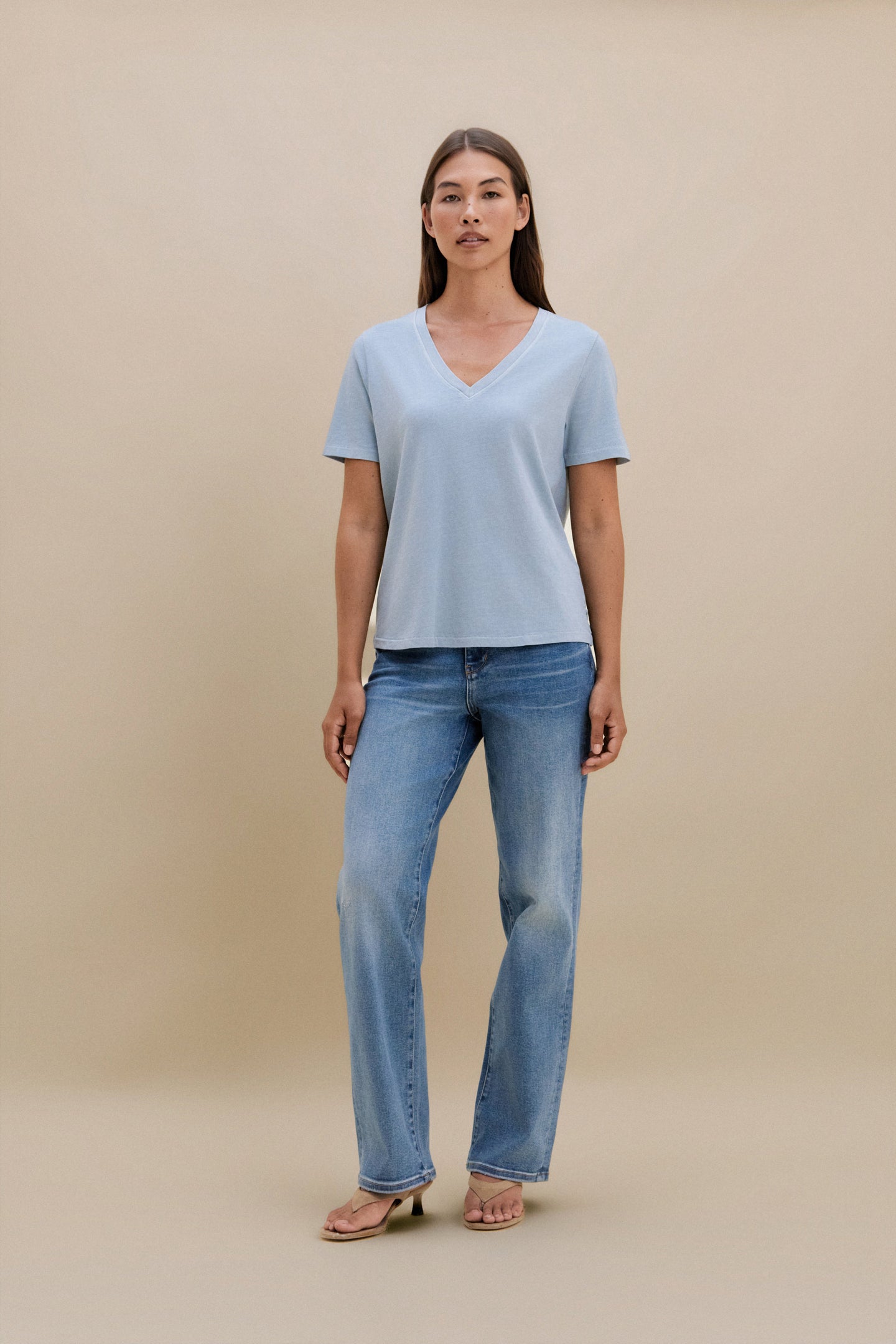 Woman wearing a light blue t-shirt and jeans on a beige background