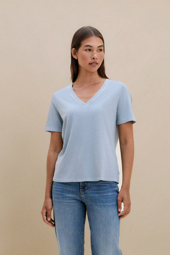 Woman wearing a blue t-shirt and jeans on a beige background | model-size: 4