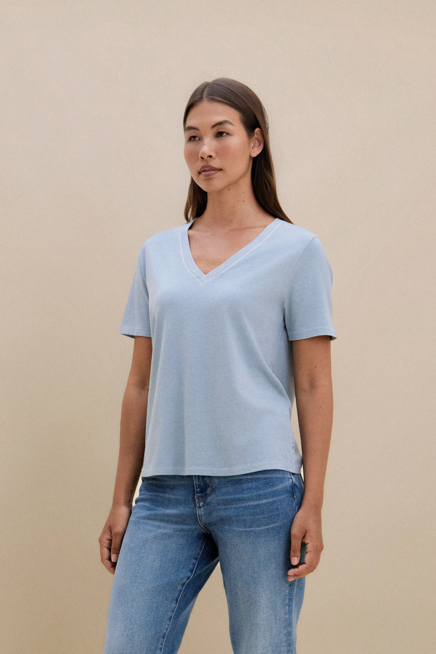 Woman wearing a light blue t-shirt and jeans against a beige background